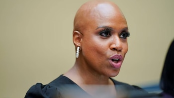 Primer plano de una mujer afroamericana calva, con pendientes de aro de perlas y un piercing en la nariz, mirando hacia la derecha y hablando