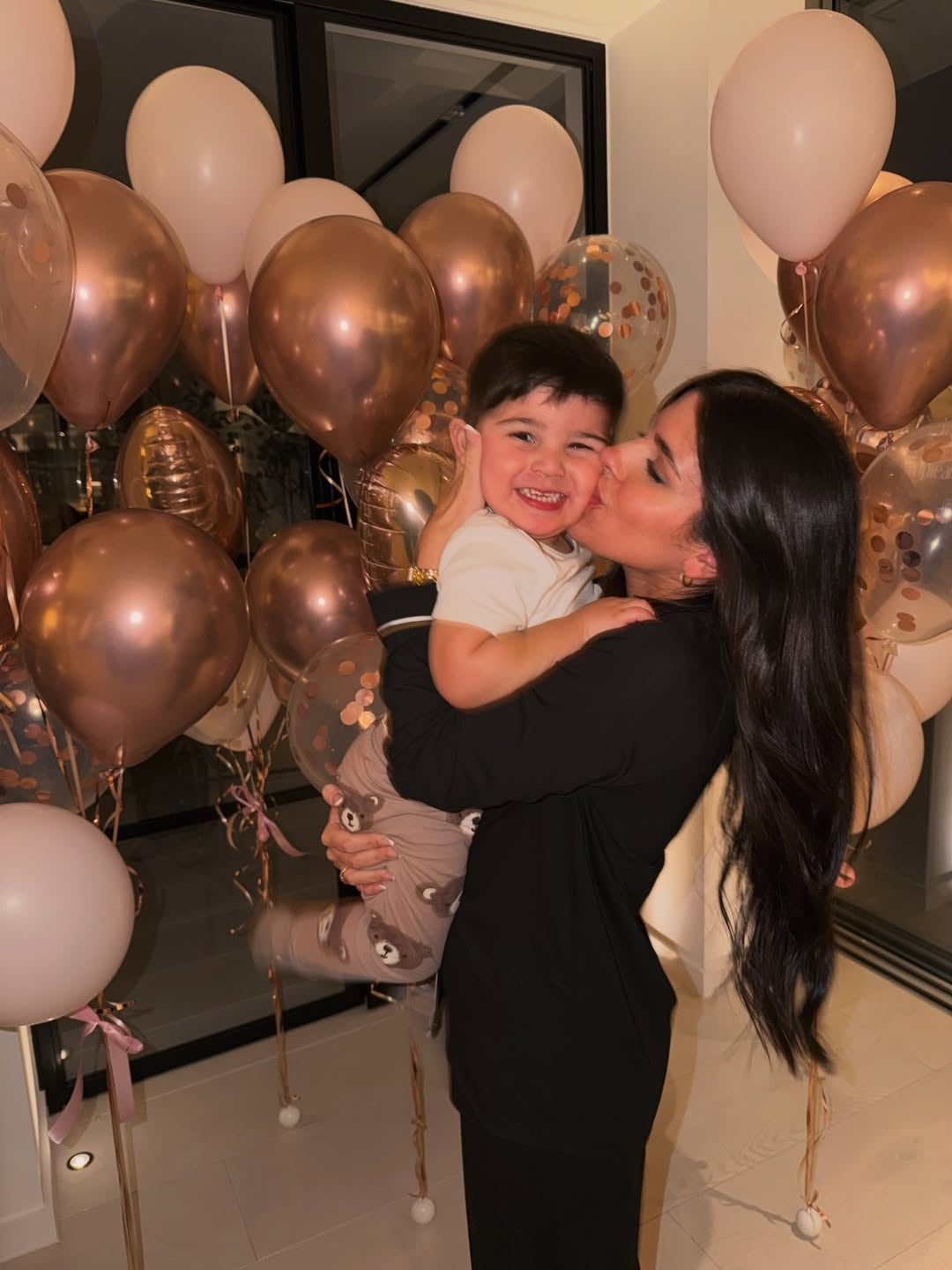 Valen sonríe mientras besa a su hijo pequeño, que ríe con deleite, rodeados de globos de colores rosados y dorados que celebran un momento especial (Instagram: valucervantes)