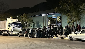 Personas reunidas de noche junto a un camión Scania blanco, automóviles y una entrada con un cartel de Arata