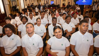 Jóvenes sentados en un auditorio visten camisetas polo blancas con un pequeño emblema verde en el pecho