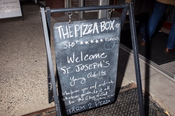 Un cartel da la bienvenida a los feligreses a un evento social previo a la misa en el Pizza Box. (Brian Anselm/Para The Washington Post)