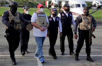Un hombre esposado camina por una pista aérea rodeado por agentes uniformados con chalecos tácticos frente a una avioneta