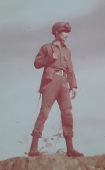 Fotografía vintage con tono rojizo de un soldado en uniforme militar, casco con gafas, de pie en un terreno irregular contra un cielo liso