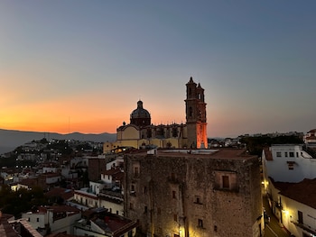 Vista aérea de un pueblo colonial mexicano al atardecer, con una gran iglesia barroca de dos torres en el centro y un cielo naranja y azul