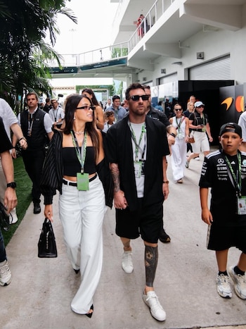 Lionel Messi y Antonela Roccuzzo caminan de la mano en el paddock del Gran Premio de Miami, su hijo visible a la derecha, entre una multitud y vegetación