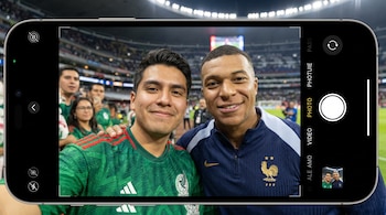 Selfie en primera persona de un teléfono mostrando a un fan con camiseta de México y Kylian Mbappé con chaqueta de Francia, sonriendo. Fondo de estadio desenfocado.