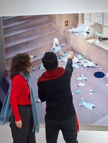 Dos personas de espaldas observan una imagen de gran tamaño con piezas de cerámica rota sobre unas escaleras
