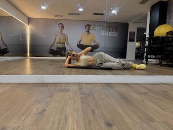 Una mujer recostada en el suelo de un gimnasio se toma una foto frente a un espejo con su teléfono móvil