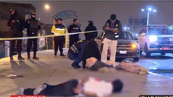 Agentes policiales y personal de investigación en una escena nocturna con dos individuos inmovilizados en el suelo, vehículos y cinta pericial