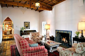 Sala de estar con chimenea encendida, sofás, mesa de centro, y un arco que conduce a una biblioteca, con techo de vigas de madera