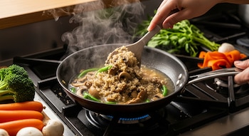 Mano removiendo quinoa, hongos y judías verdes en una sartén humeante sobre una estufa con llama azul. Vegetales frescos alrededor.