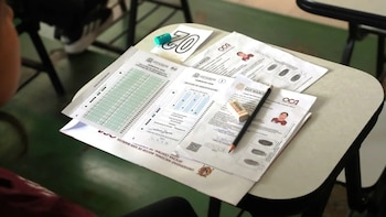 Hojas de evaluación con ficha de identificación, un carné con foto, un lápiz y un borrador sobre una carpeta escolar