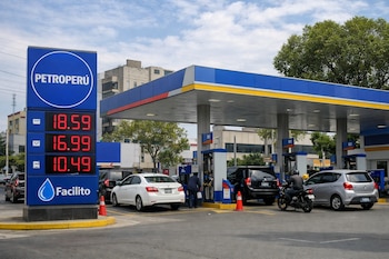 Vista diurna de una estación de servicio Petroperú en Lima con cartel digital azul mostrando precios altos. Vehículos hacen fila para cargar.