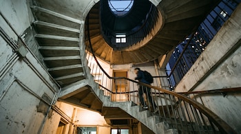 Perspectiva inferior de una escalera de caracol de concreto por la que sube una persona con mochila.