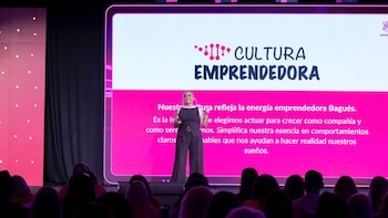 Una mujer en un escenario frente a una gran pantalla rosa con el texto "CULTURA EMPRENDEDORA" y una audiencia oscura en primer plano