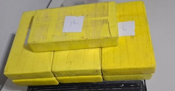 Primer plano de varios paquetes rectangulares apilados, envueltos en plástico amarillo y con etiquetas blancas que muestran los números 6 y 7