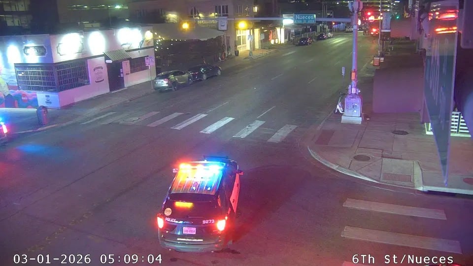 Un vehículo policial con las luces de emergencia encendidas se detiene en una calle urbana iluminada por la noche, indicando una posible intervención o vigilancia en la intersección de 6th St y Nueces (City of Austin)