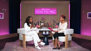 Una mujer con traje blanco y otra con blusa crema, sentadas en sillones frente a micrófonos en un estudio con un letrero de neón: 'Baby, this is Keke Palmer'