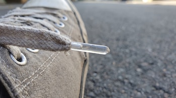 Primer plano de la punta de plástico transparente de un cordón de tela sobre una zapatilla y asfalto.