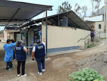 Tres personas con chalecos de inspección sanitaria y una con vestimenta médica observan el exterior de un puesto de salud en un terreno rural