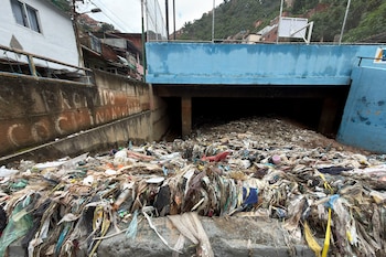 Acumulación de gran cantidad de residuos plásticos y basura frente al túnel de una quebrada bajo una estructura azul