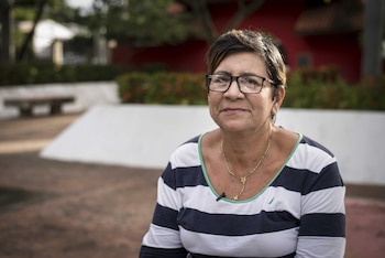 Retrato de Lady M, una mujer de cabello castaño corto y gafas, vestida con una camiseta de rayas y un collar dorado con una cruz, sentada al aire libre