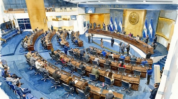 Acuarela de un hemiciclo legislativo. Se ven asientos azules, personas sentadas y de pie, banderas de El Salvador y un escudo nacional en el fondo.