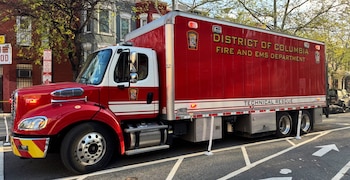 Gran camión de rescate técnico rojo y blanco del Departamento de Bomberos y EMS del Distrito de Columbia con luces intermitentes, estacionado en una calle