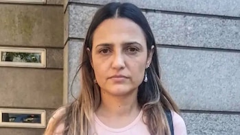 Retrato de Mercedes Trimarchi, una mujer con cabello castaño oscuro a claro, expresión neutral, usando pendientes colgantes y una camiseta rosa, fondo de pared gris