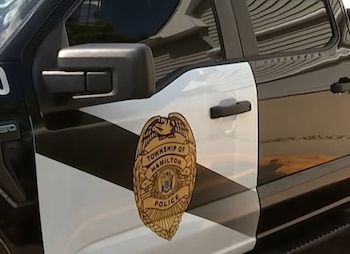 Costado de una camioneta policial de color negro y blanco con la insignia dorada de la Policía del Municipio de Hamilton