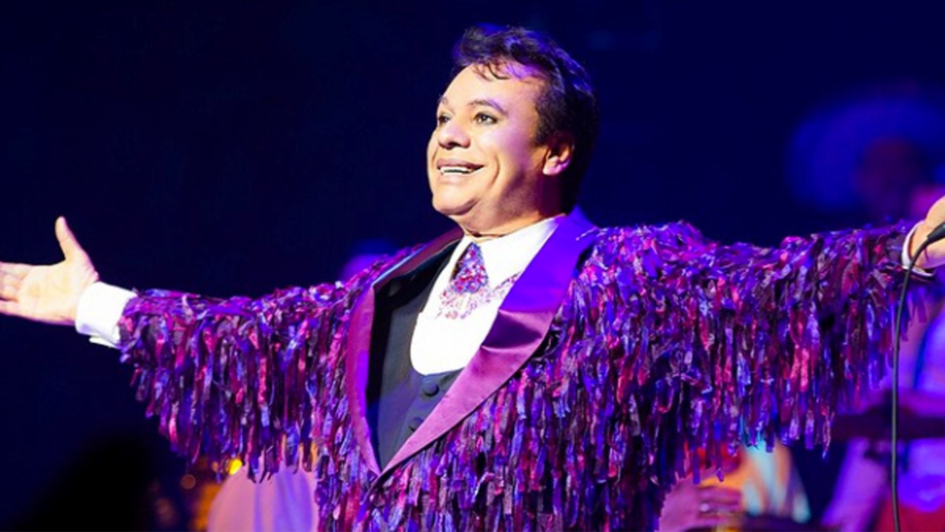 Juan Gabriel sonríe en el escenario con un llamativo atuendo morado, anticipando el Tributo Sinfónico en su honor que llega a Lima.