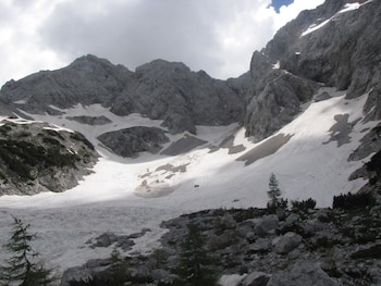 Un paisaje montañoso con laderas rocosas grises cubiertas de nieve y pequeños pinos en la parte inferior