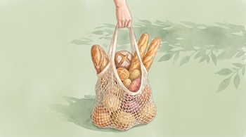 Una mano sostiene una bolsa de red con baguetes, panes redondos, papas y camotes sobre un fondo de tono verde.