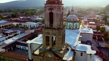 Vista aérea de la torre y cúpula de una iglesia rodeada por casas bajas y colinas al fondo