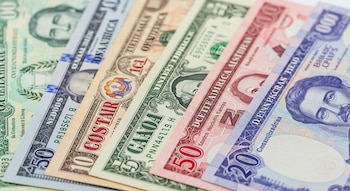 Vista cercana de billetes de quetzales, dólares estadounidenses, colones, balboas y pesos dominicanos apilados y parcialmente superpuestos.