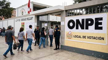 Personas caminando hacia la entrada de un centro educativo decorado con pancartas electorales y custodiado por agentes policiales.