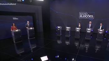 Un estudio de televisión con personas detrás de atriles frente a una pantalla con el texto Band Eleições