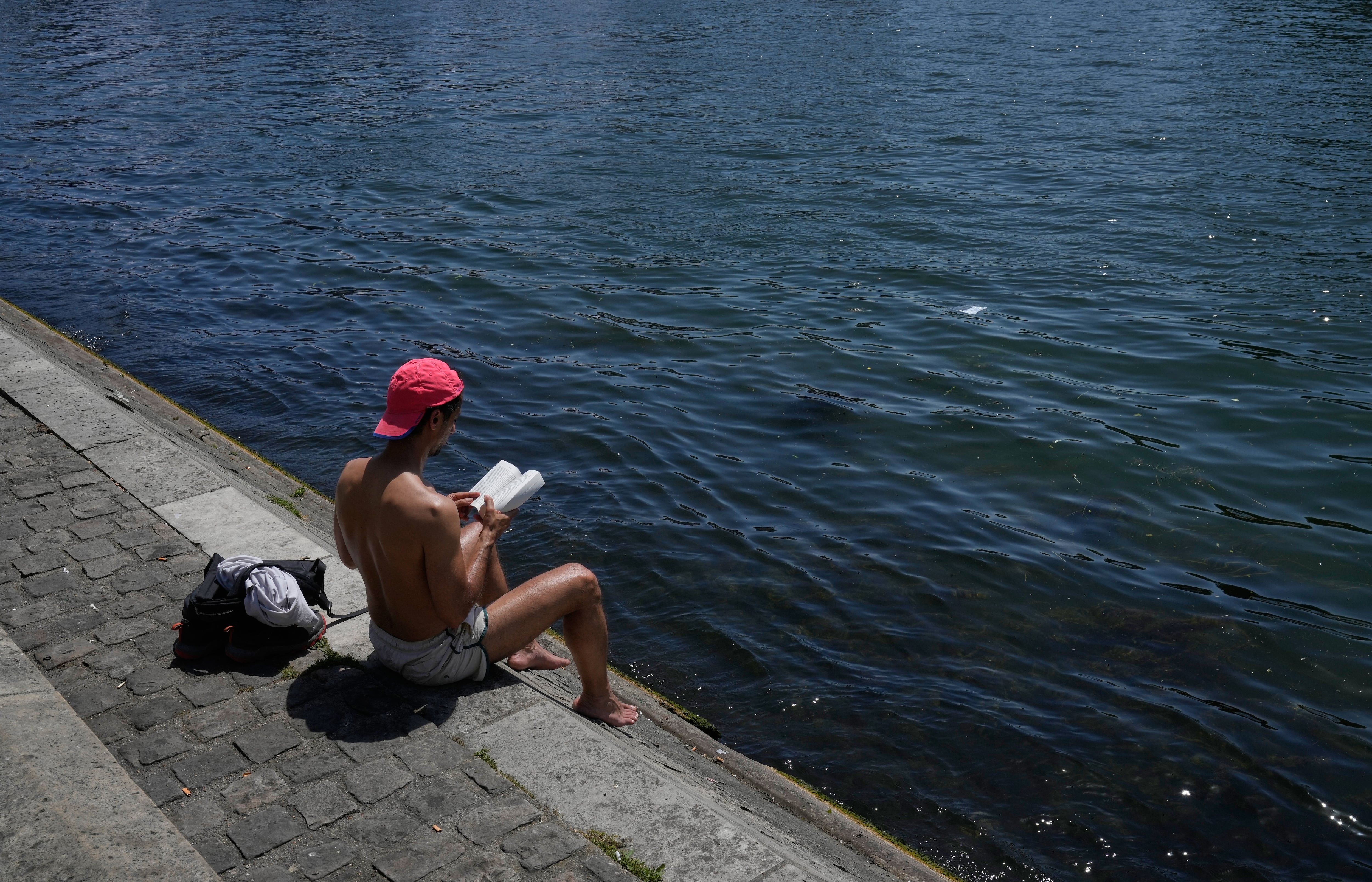 Un hombre lee un libro sentado al sol a orillas del río Sena, el lunes 25 de mayo de 2026, en París. (AP Foto/Michel Euler)