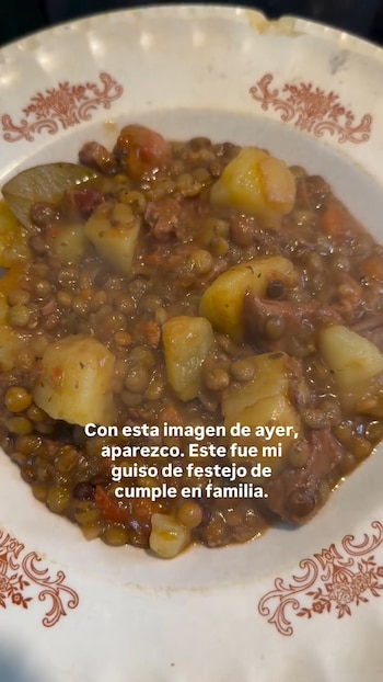 Primer plano de un plato blanco con borde decorado, conteniendo un guiso humeante de lentejas, trozos de papa y carne en una salsa espesa y oscura