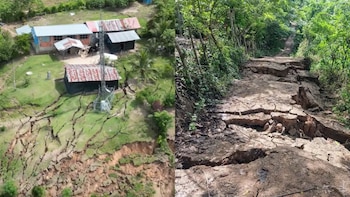 La imagen muestra un terreno rural con grietas extensas junto a casas y una torre de comunicación, y un camino de tierra severamente fracturado en un área boscosa