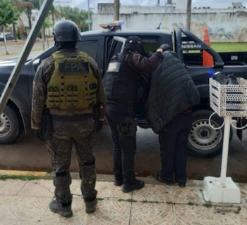 Dos agentes con chalecos tácticos marcados con la sigla FPA introducen a una persona encapuchada en una camioneta policial