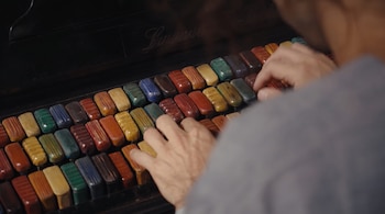 Primer plano de manos de una persona sobre las teclas de un instrumento musical. Las teclas son rectangulares, texturizadas y de diversos colores en hileras.