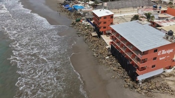 Vista aérea de la costa donde las olas del mar llegan a la base de edificios protegidos por un muro de rocas