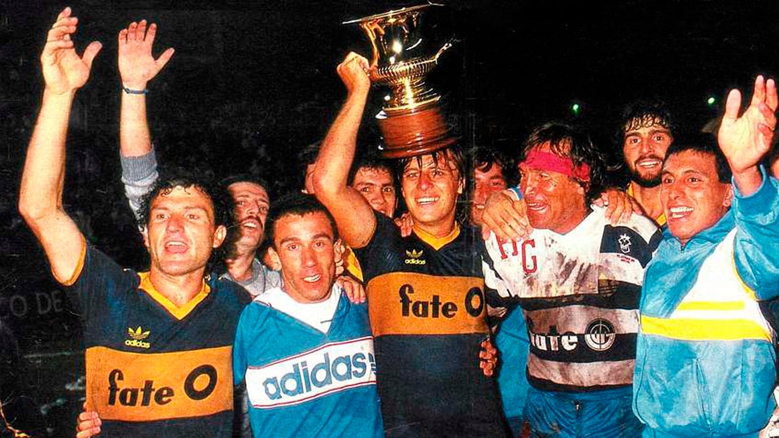 Jugadores de Boca Juniors y otros festejando un campeonato, levantando una copa dorada en una noche de celebración, reflejando una era del fútbol con Fate como patrocinador. (Picryl)