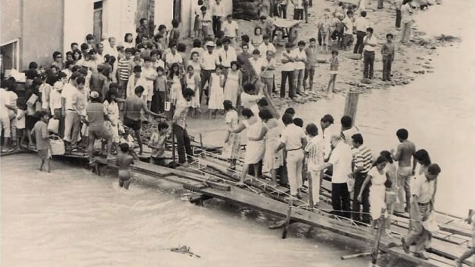 Residentes de Piura, Perú, atraviesan una pasarela de madera sobre aguas desbordadas por el fenómeno El Niño de 1982-1983, que afectó la infraestructura local y la vida de millones. (Universidad de Piura)