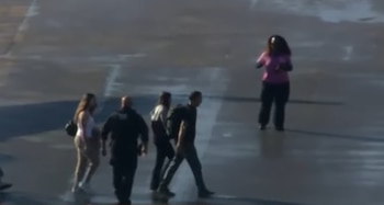 Cuatro personas caminan sobre el asfalto de una pista exterior cerca de una mujer con camiseta rosa que permanece de pie