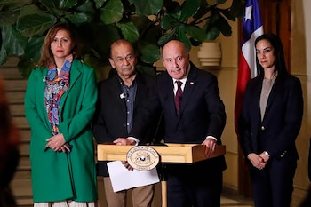 Cuatro personas, dos hombres y dos mujeres, frente a un podio de madera con el escudo del Senado de Chile, y una bandera chilena al fondo