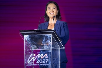 Keiko Fujimori sonríe y habla desde un podio transparente con los logos de Lima 2027 y Panam Sports, frente a un fondo magenta degradado