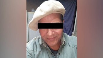 Primer plano de Oscar Jégou usando una boina clara y camisa de mezclilla; sus ojos están censurados con una barra negra. El fondo es un interior oscuro
