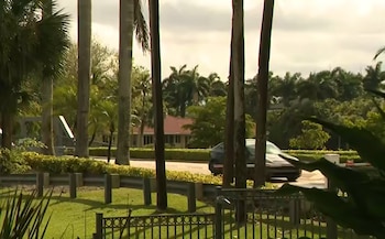 Un SUV oscuro o minivan transita por una calle residencial bordeada de palmeras y exuberante vegetación tropical en Weston, Florida